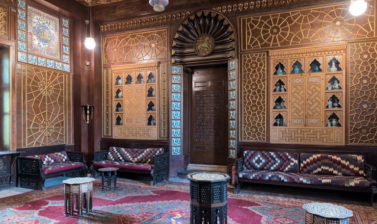 Cairo, Egypt - December 2 2017: Manial Palace of Prince Mohammed Ali. Guests Hall with wooden ornate ceiling, wooden ornate door, lanterns, colorful ornate couches, tea tables and ornate carpet